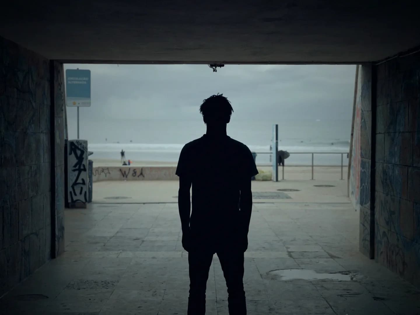 A man in silhouette framed dead centre at the end of a concrete underpass.