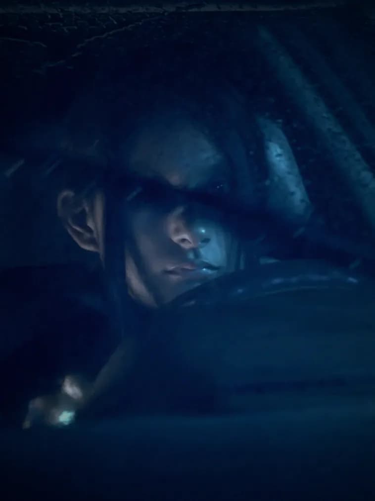 A woman behind a wet car window, graded in the series' blue.