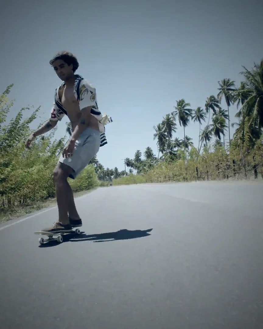A skateboarder carving down an empty road lined with palms.