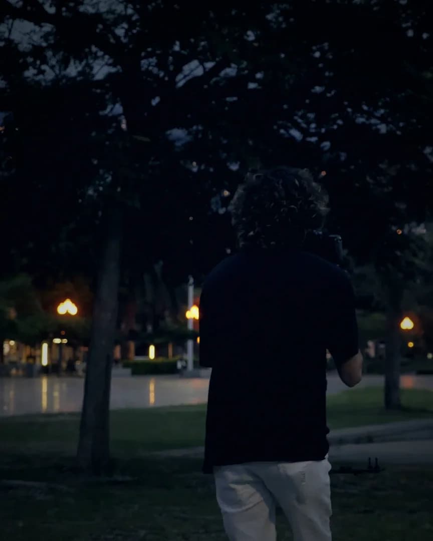 A camera operator filming a park at dusk, city lights beyond.