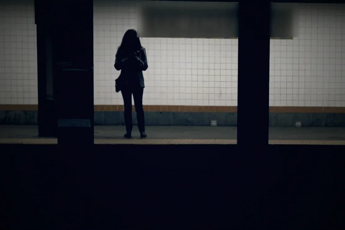 The same woman on the platform, graded dark and blue like a night-time drama.
