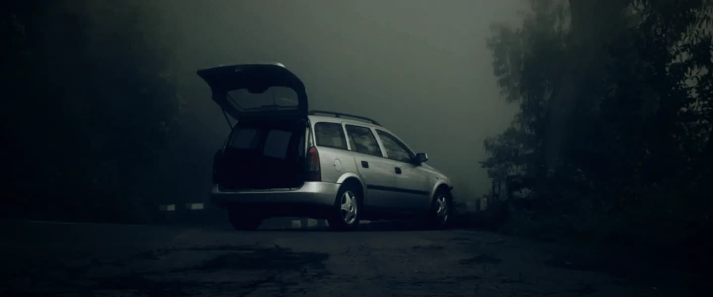 A silver estate car parked on a foggy roadside, its boot open.