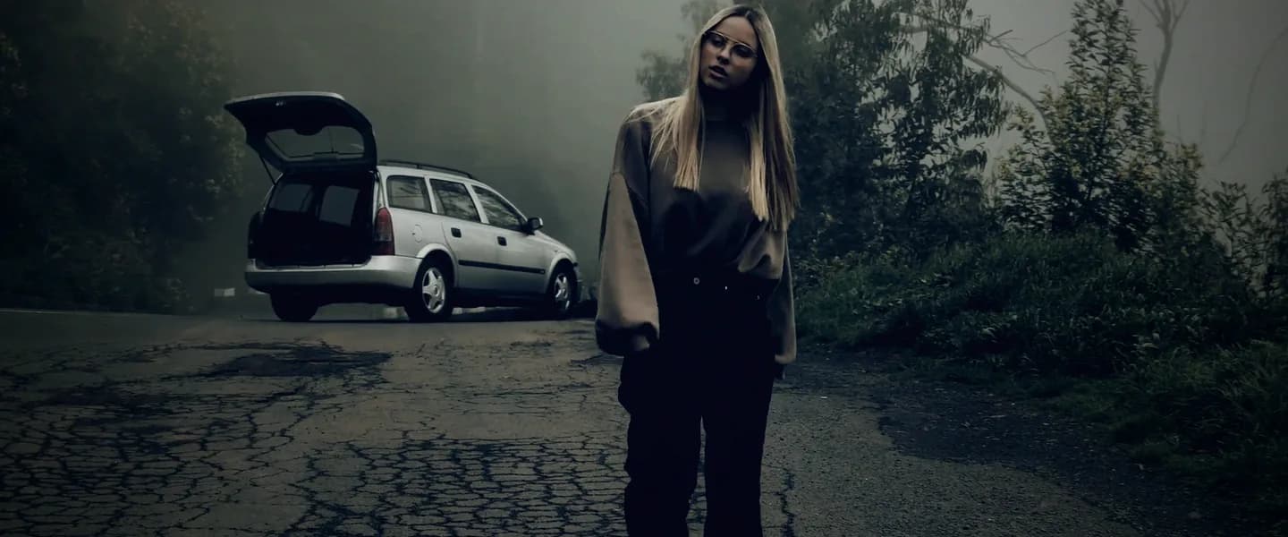 The woman pausing in the road, the car behind her in the fog.