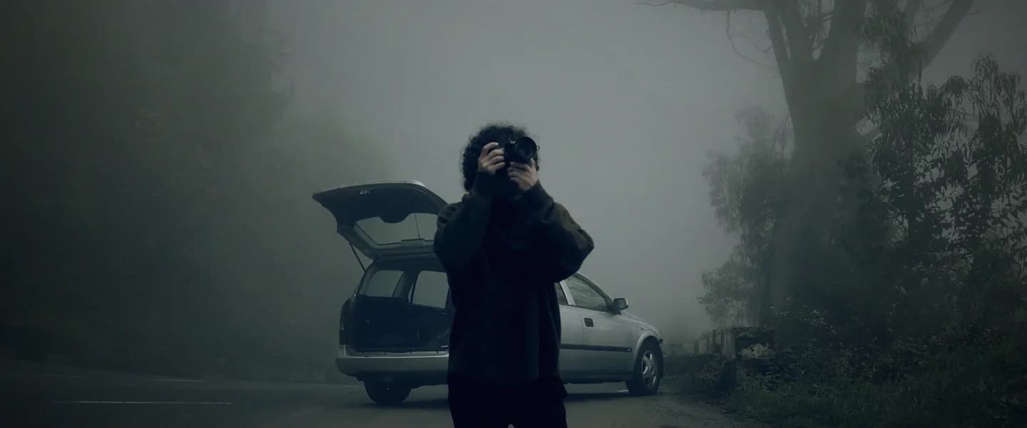 A young man raising his camera in front of the car.