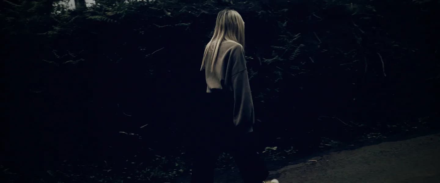 The woman walking on along a dark roadside wall.